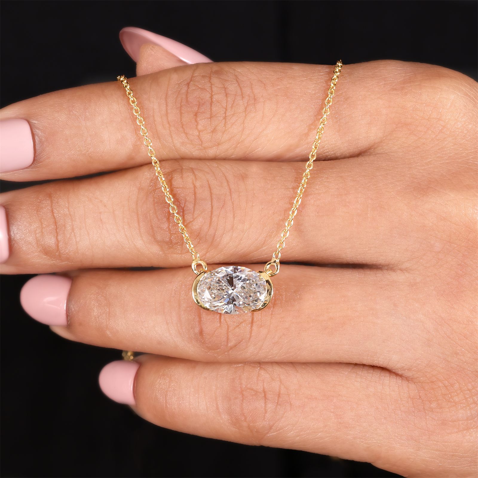 An oval laboratory-grown diamond pendant held in the hand